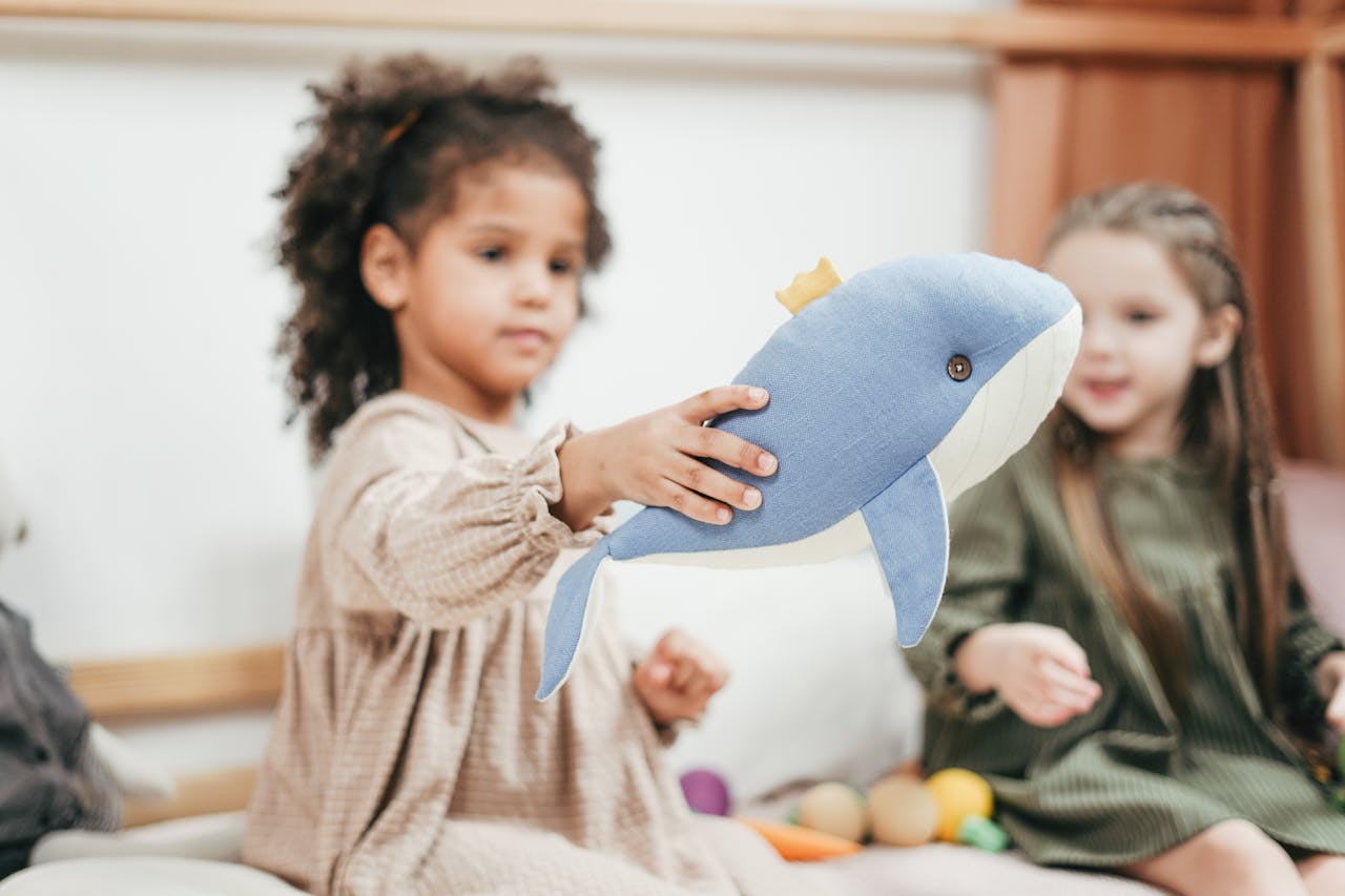 Two young girls playing with a whale stuffed toy indoors, showcasing a happy childhood moment.